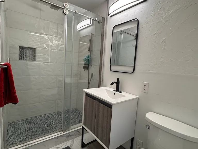 Fully renovated primary bathroom featuring a frameless glass walk-in shower, premium textured tile, custom mosaic accents, and a luxury Delta rain shower system with a convenient hand wand.