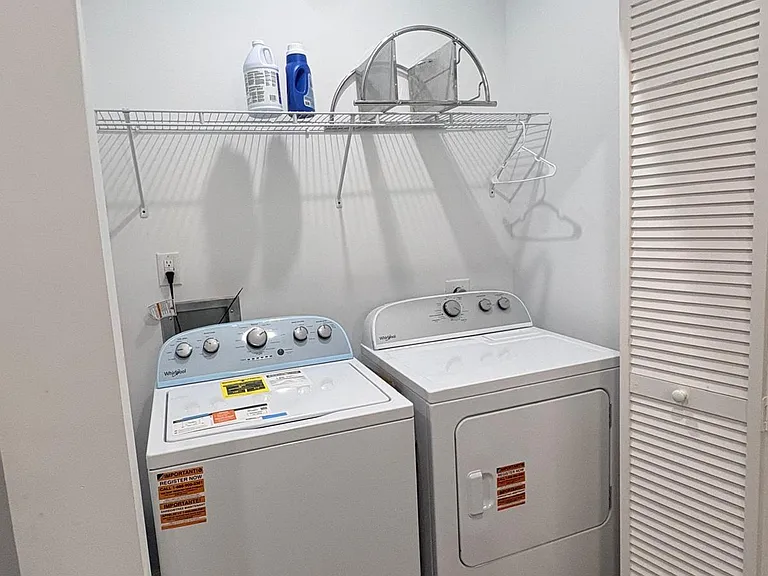 Dedicated laundry closet with full-size washer and dryer plus an overhead wire shelf for supplies and storage.