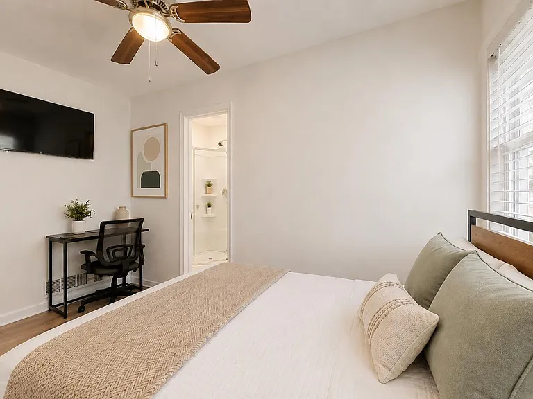 Bedroom features a queen bed, large window with blinds, ceiling fan, wall-mounted TV, and a dedicated desk workspace.