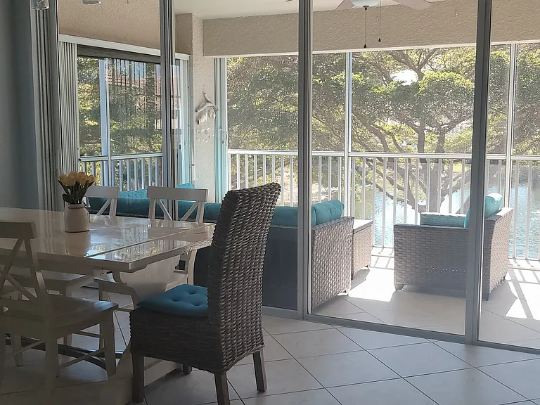 The open-concept dining area and lanai create a seamless indoor-outdoor living experience. Enjoy lake views through sliding glass doors while dining at a coastal-chic table with wicker seating. The screened lanai offers additional lounging space.