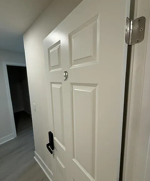 Interior hallway with paneled door, neutral walls, and durable flooring connecting to adjacent rooms.