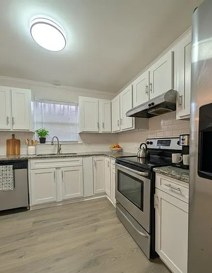 U-shaped kitchen with white cabinetry, ample granite-look counters, stainless appliances, and a window over the sink.