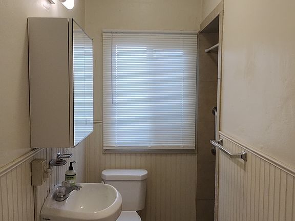 Tiled bathroom has pedastal sink and bright lighting. Back window is vinyl with obscure glass.