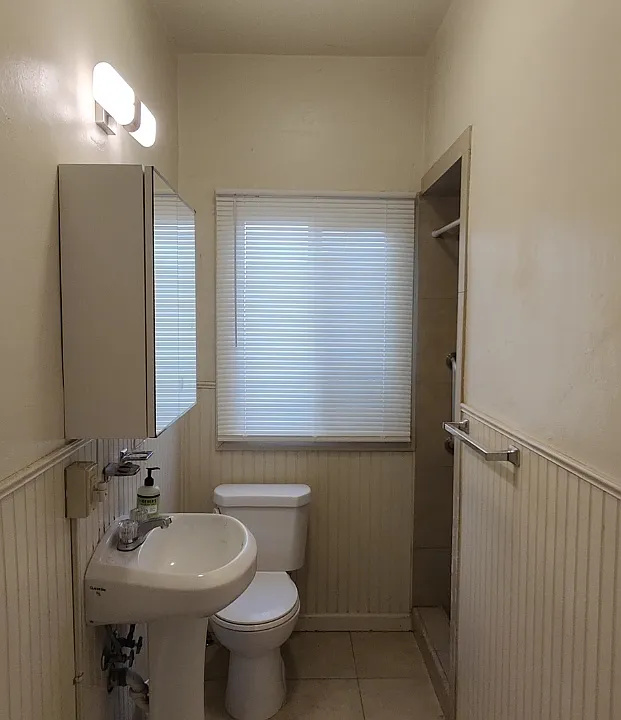 Tiled bathroom has pedastal sink and bright lighting. Back window is vinyl with obscure glass.