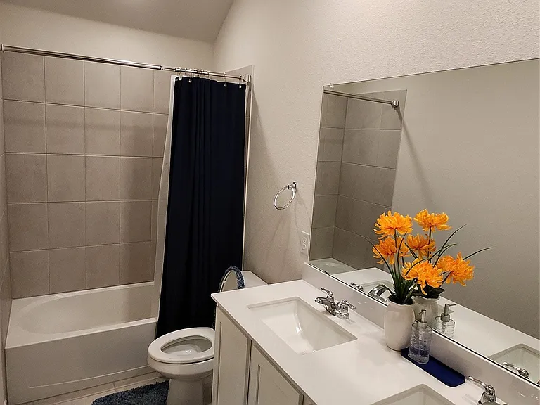 Bathroom featuring a dual vanity with white cabinetry and integrated sinks, a full-width mirror, and a bathtub with tile surround