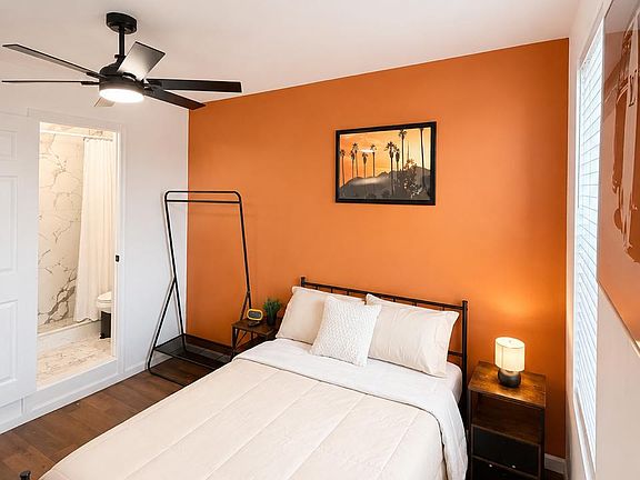Private bedroom featuring a full bed, ceiling fan, nightstands with lighting, and a window with blinds; private bathroom