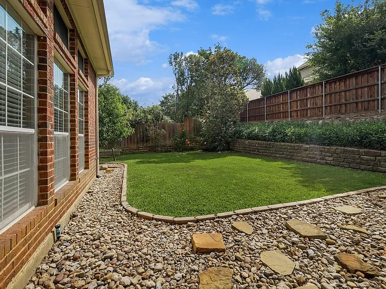 Rear exterior featuring a manicured lawn, stone retaining wall, and a full privacy fence
