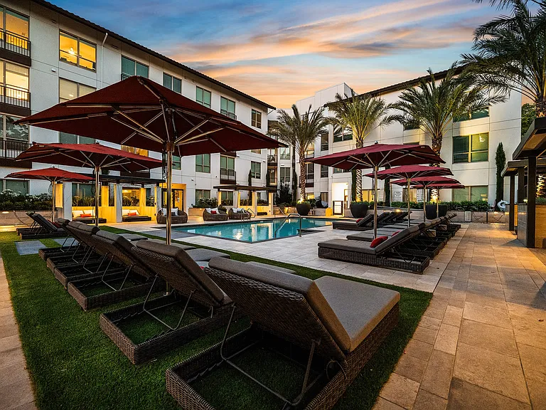 Poolside retreat with red umbrellas, loungers, and sunset backdrop