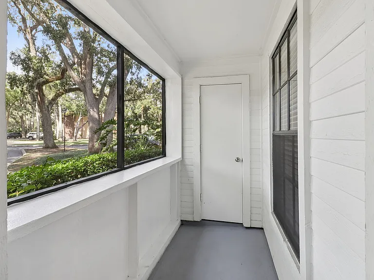 Inviting enclosed porch with large windows showcasing a serene view of lush trees, perfect for relaxing and enjoying nature.