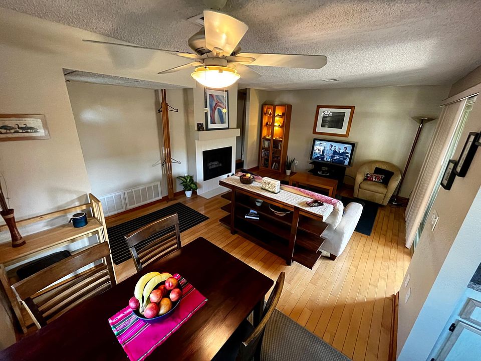 Living room (wooden floor, sofa, armchair, coffee table, fireplace, dinner table) with large windows and access to patio