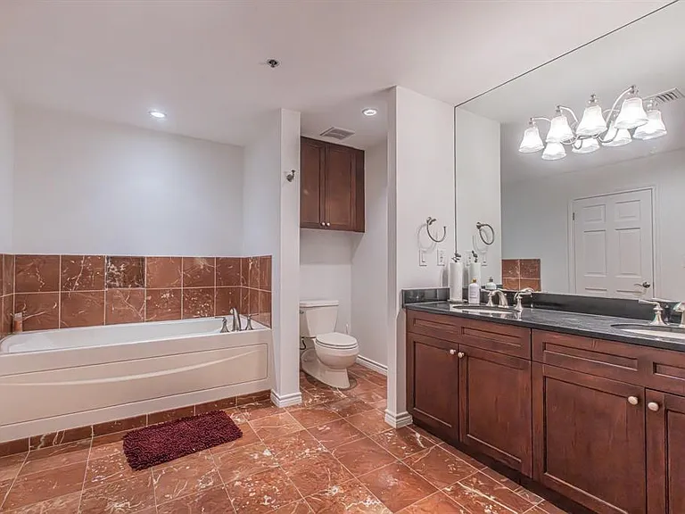 Bathroom featuring a built-in tub with tile surround, a dark wood-finish double vanity with dual undermount sinks and dark countertop, and a large wall-mounted mirror