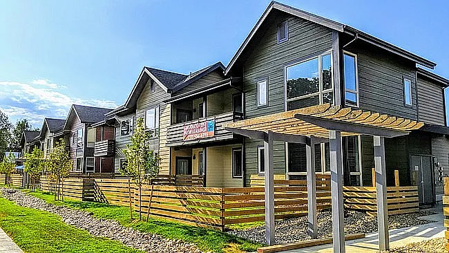Charming modern apartments with inviting exteriors, featuring wooden fencing and a lush green landscape under a clear blue sky.