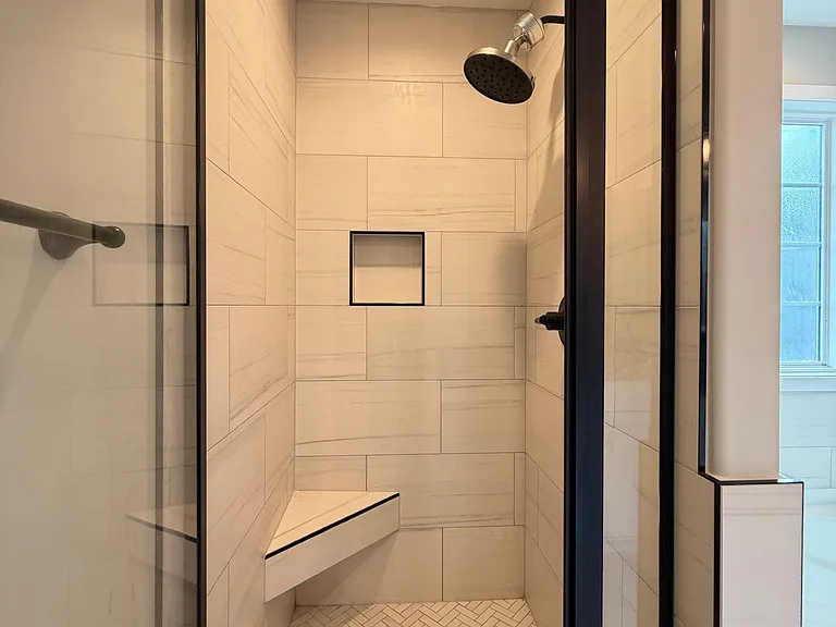 Walk-in shower with tile surround, built-in niche and bench, and a glass enclosure with a rainfall-style showerhead.