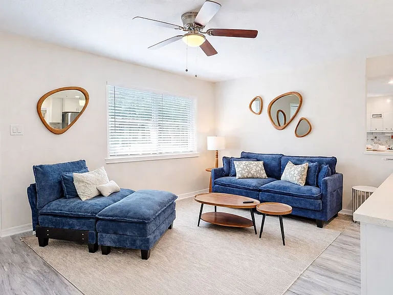 Beautifully furnished shared living room with plush blue sofas, decorative mirrors, and open kitchen access