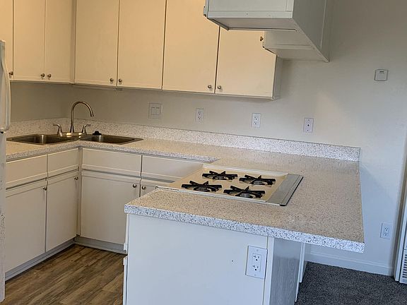 Kitchen with plank style flooring, white cabinets, and gas range at Carlsbad Sunset Senior Apartments in Carlsbad, California.