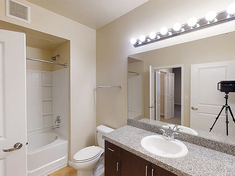 Apartment bathroom with granite countertops and white tiles and features.