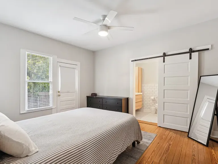 Primary bedroom. Door opens onto steps to the side of the backyard running along Hawthorne Ave. Sliding barn door leads into bathroom. Closet runs the length of the right side of the room.