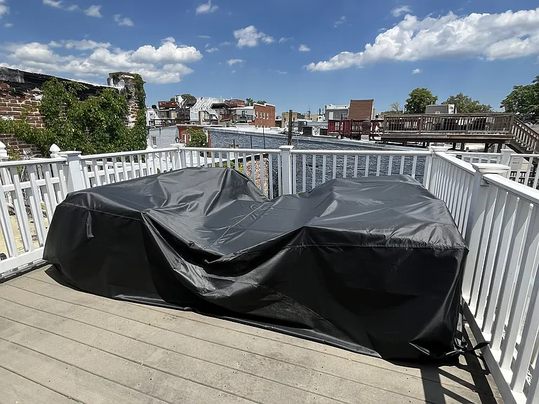Outdoor roof deck with covered furniture (couch, chairs, and table), with view of the city