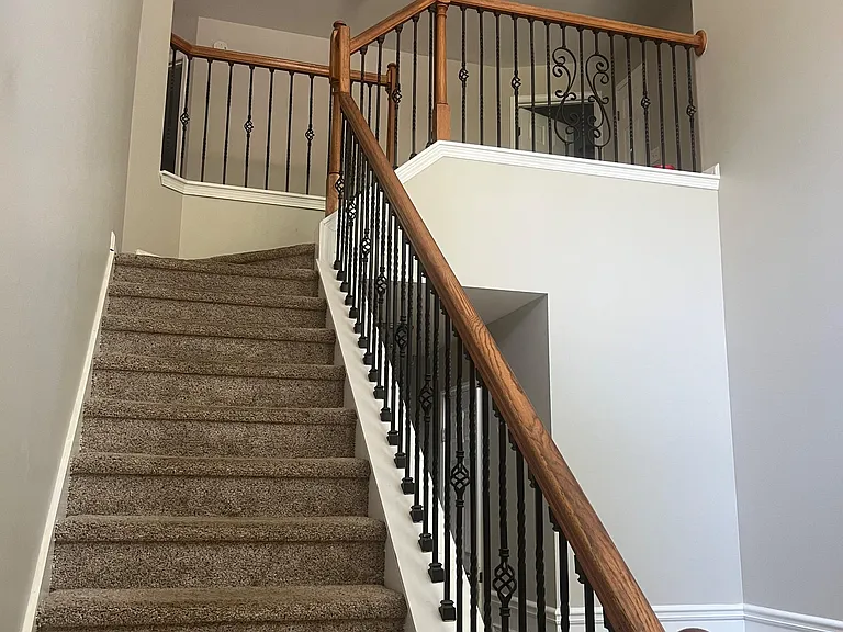 Carpeted staircase with wood handrails and wrought-iron balusters leads to an open upstairs landing and hallway access.