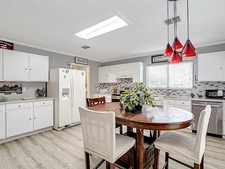 Eat-in kitchen with ample white cabinetry, tile backsplash, full appliance suite, and a dining table under pendant lighting.