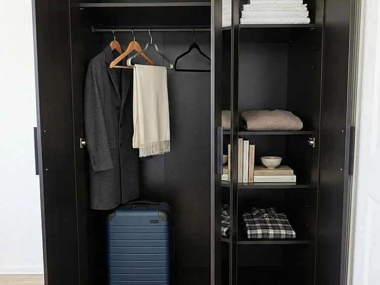 Tall wardrobe with hanging rod and multiple shelves provides convenient storage for clothing, linens, and luggage.
