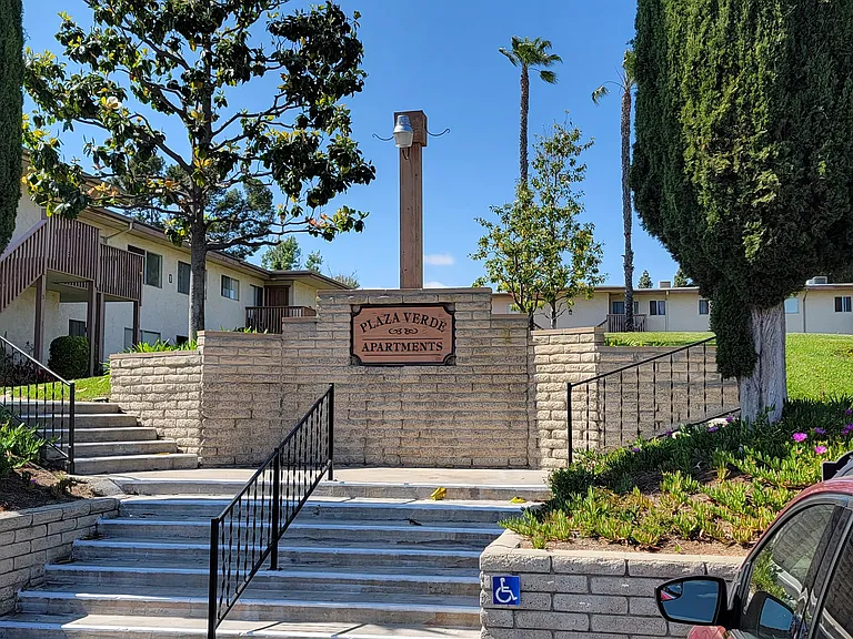 Parking lot steps to apartment walkways with mature landscaping and lots of grassy open space at Plaza Verde Apartments in Escondido, California.
