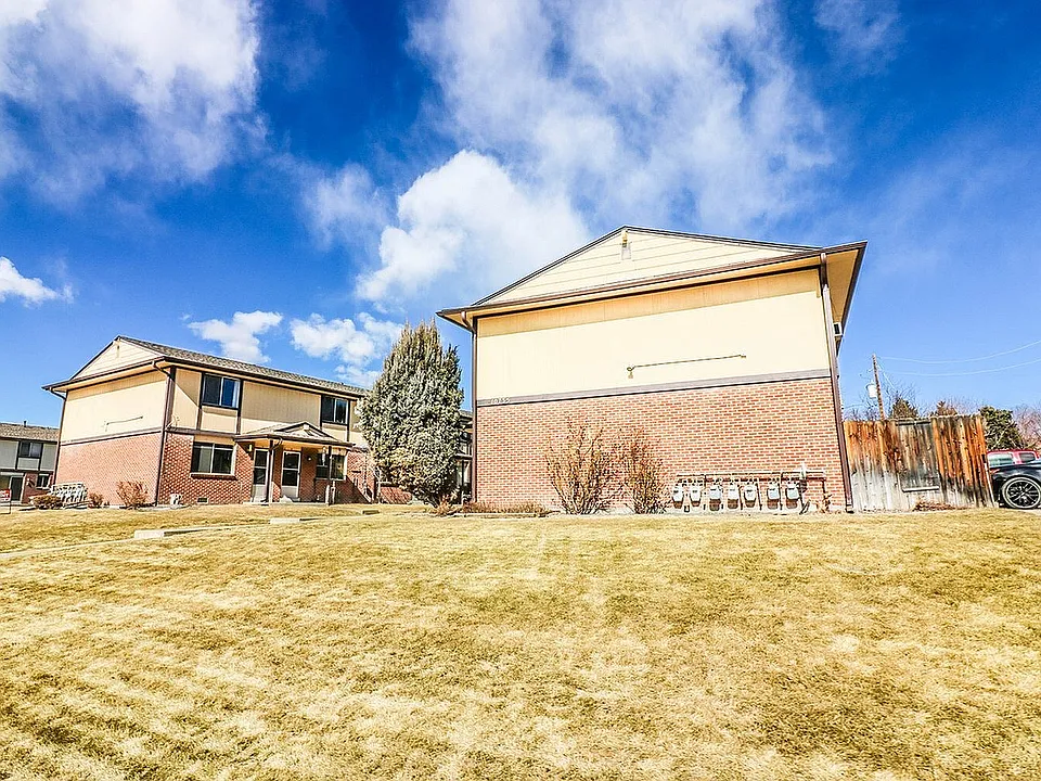 Charming two-story brick and siding apartment complex with a spacious lawn under a bright blue sky.