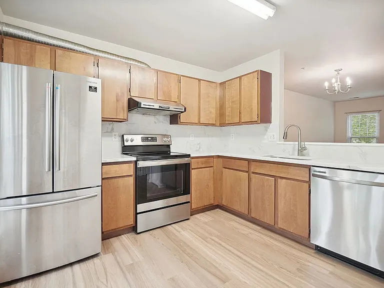 Overview of the kitchen and its stainless-steel appliances with the living and dining area visible beyond through the pass-through opening.