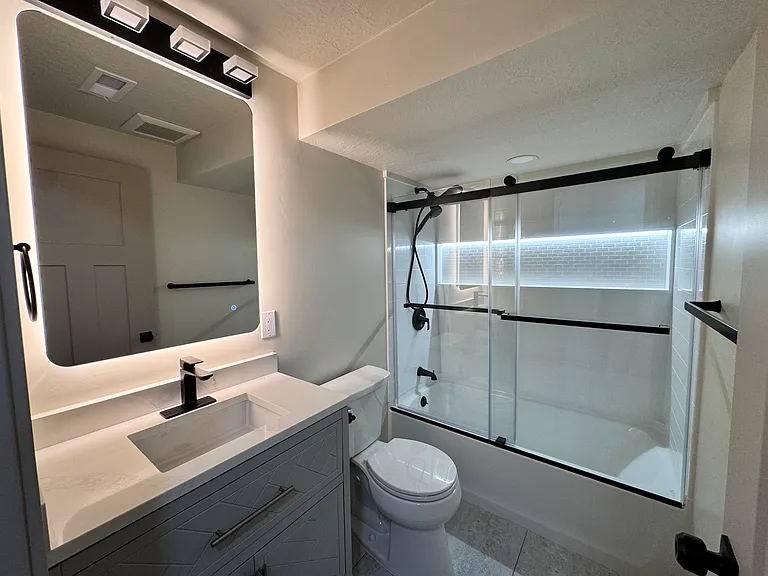 New bathroom featuring a modern vanity, LED-lit anti-fog mirror, and a tub/shower combo with sliding glass doors.