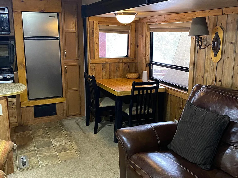 Living room that contains a small table, full apartment refrigerator, stove and cooktop, microwave, Smart TV and a leather loveseat.