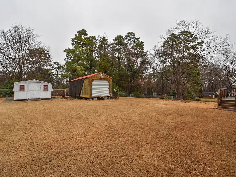 Fenced backyard with lawnmower shed and building with electricity