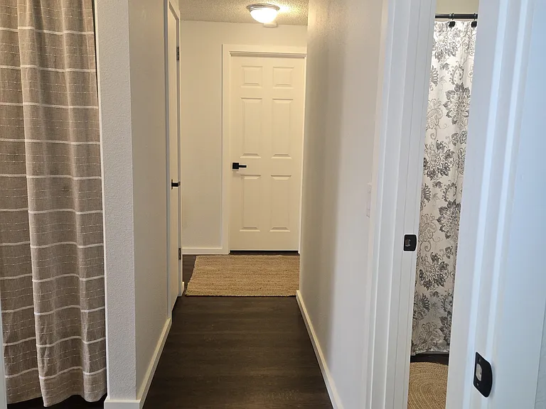 View from N. bedroom towards S. bedroom. Bathroom to right. Laundry/kitchen to left. (curtains, rugs not included).