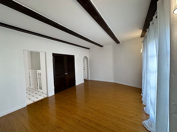 The living room is bright and spacious, featuring elegant beamed ceilings and large French windows that flood the space with natural light. Classic hardwood-style floors add warmth and charm, while the open layout provides a cozy yet airy atmosphere.