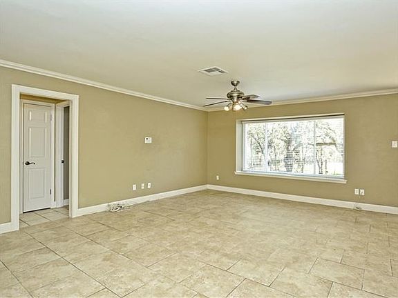Living room is spacious and has ceiling fan, staggered tile flooring and crown molding.