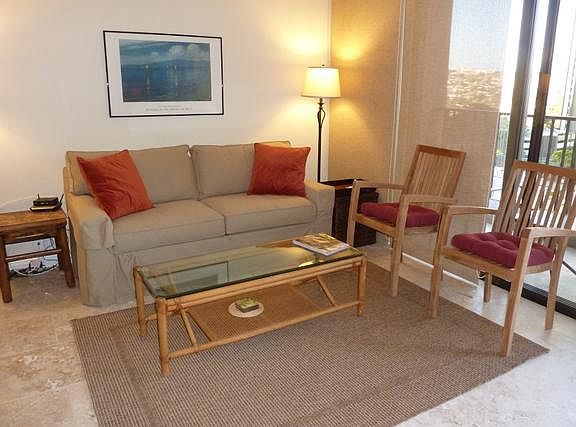 Living area with sofa, coffee table, chairs next to kitchen dining counter and view looking out lanai..