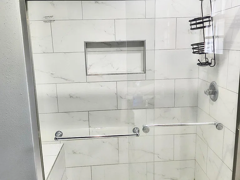 Walk-in shower with a glass enclosure, large-format tile surround, built-in shampoo niche, and pebble-style floor.