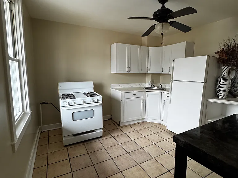 Kitchen includes stove and fridge as well as bar height, dining table. Vantage point is taken in front of the balcony door.