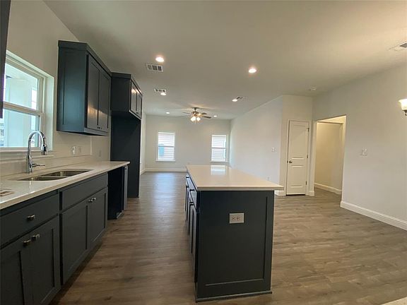 Kitchen featuring a kitchen island, a ceiling fan, dark wood finished floors, recessed lighting, and light stone counters