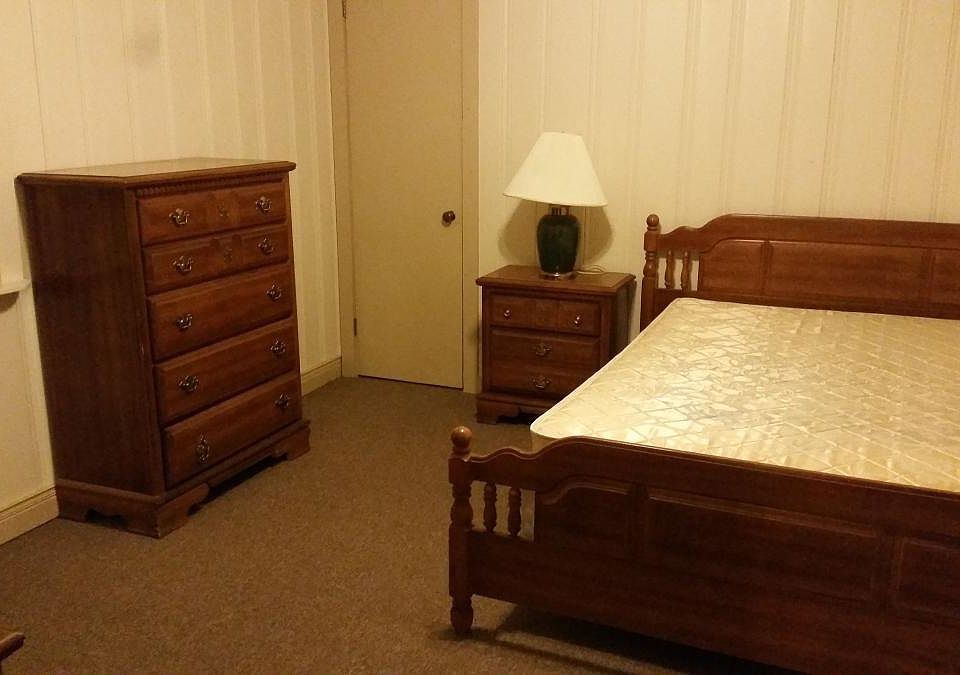 Bedroom has two dressors, full-sized bed, and side table.