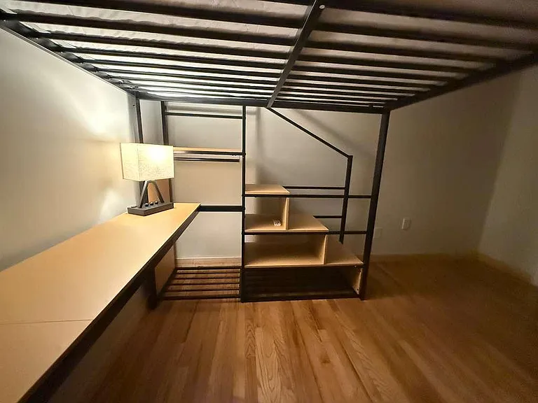 Loft-style sleeping area with wood-look flooring and built-in shelving, plus a long surface for work or storage.