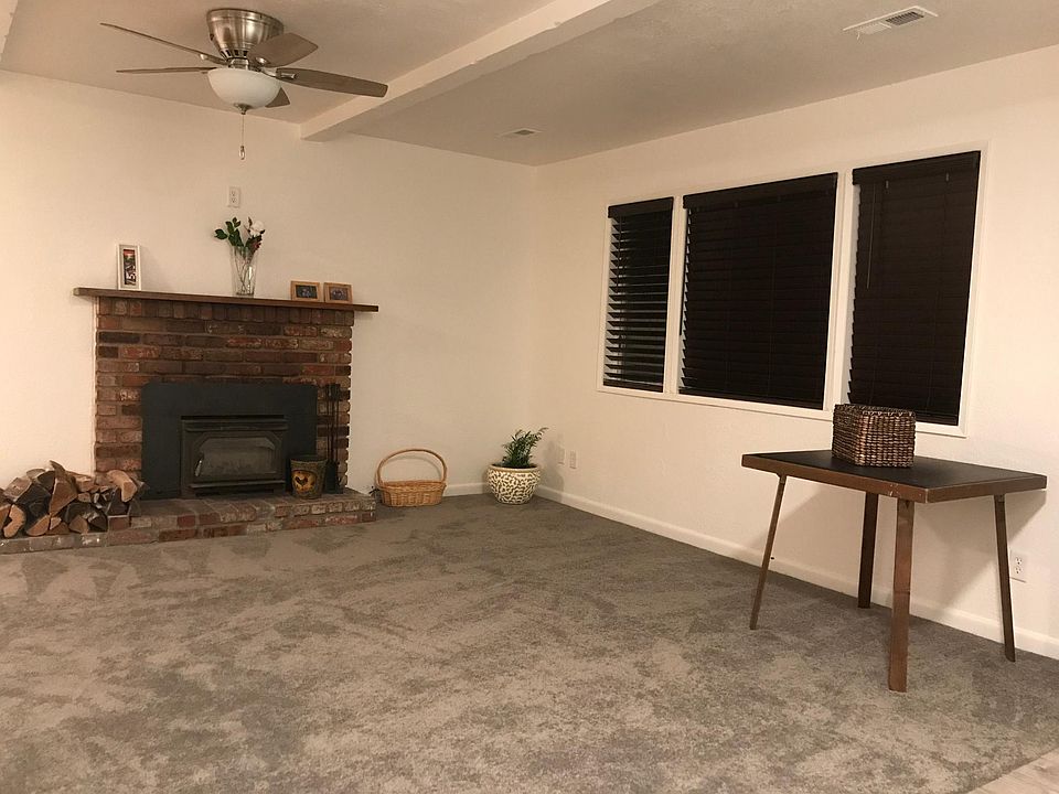 Living room with woodburning stove insert, carpet, mantel and ceiling fan.