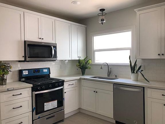 Eat-in kitchen has gray tile floors, white maple shaker cabinets, bronze hardware, stainless steel appliances including gas stove, microwave hood, dishwsher, counter depth french door refrigerator. Quartz counter tops, white subway tile backsplash.