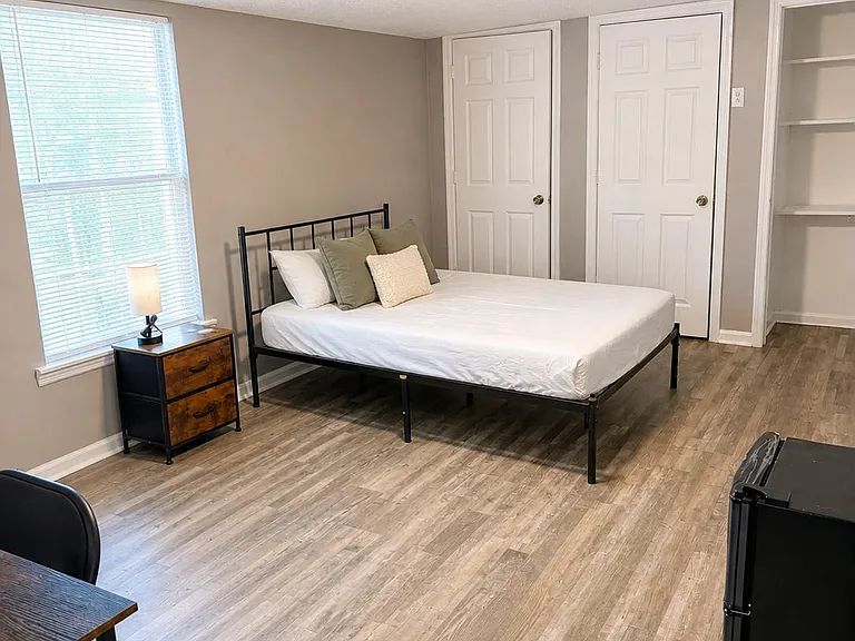 Spacious bedroom with a large window, bed, nightstand, desk area, and generous closet/storage space.