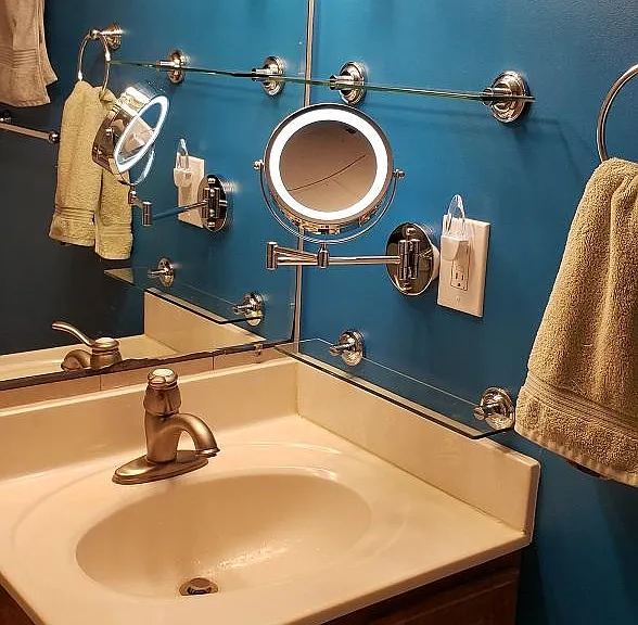 Bathroom sink with glass shelves and extendable lighted mirror that flips between magnified and regular views.