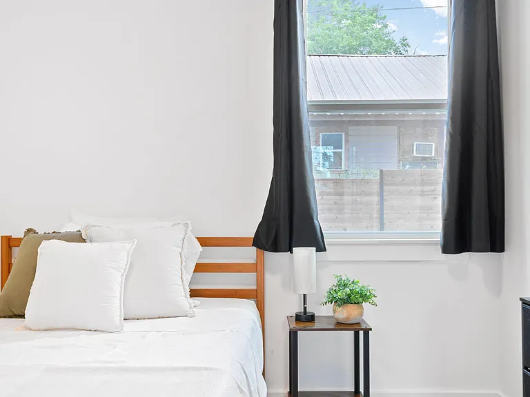 Bedroom with a full bed, side table with lamp, and a window with blackout curtains for added privacy and light control.