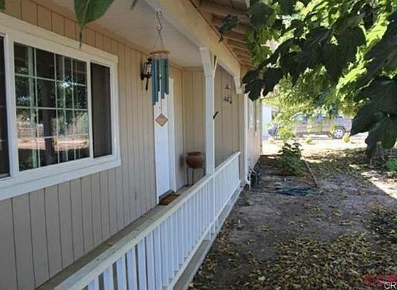 Covered front porch entrance, shaded by large trees.