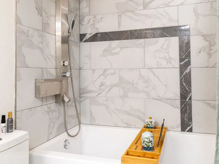 This refreshed bathroom features a sleek vanity with soft lighting and a relaxing shower-tub combo with marble-style tile. Thoughtfully stocked with essentials for a comfortable and easy stay.