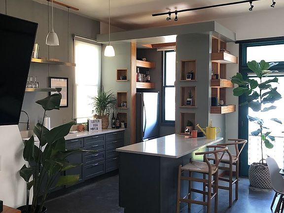 View of the Kitchen Island and Open Pantry-Refrigerator Area. Plenty of Daylight. Windows and Doors with Roll Up Shades. Silestone counter at island and kitchen
