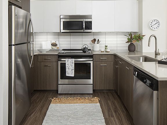 Apartment kitchen with stainless steel appliances, quartz countertops, and wood-style flooring.
