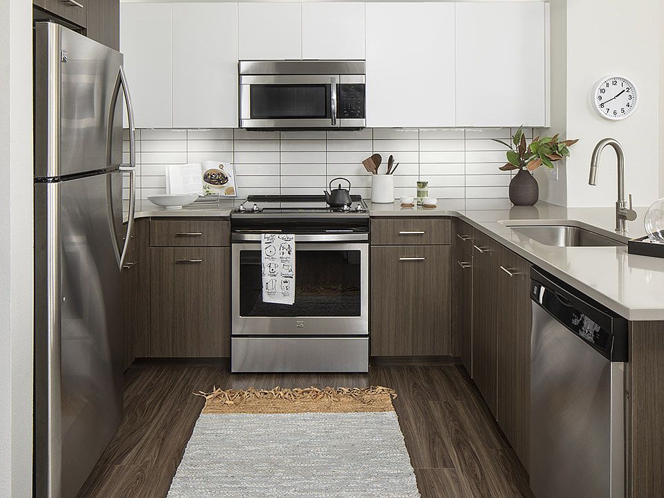 Apartment kitchen with stainless steel appliances, quartz countertops, and wood-style flooring.
